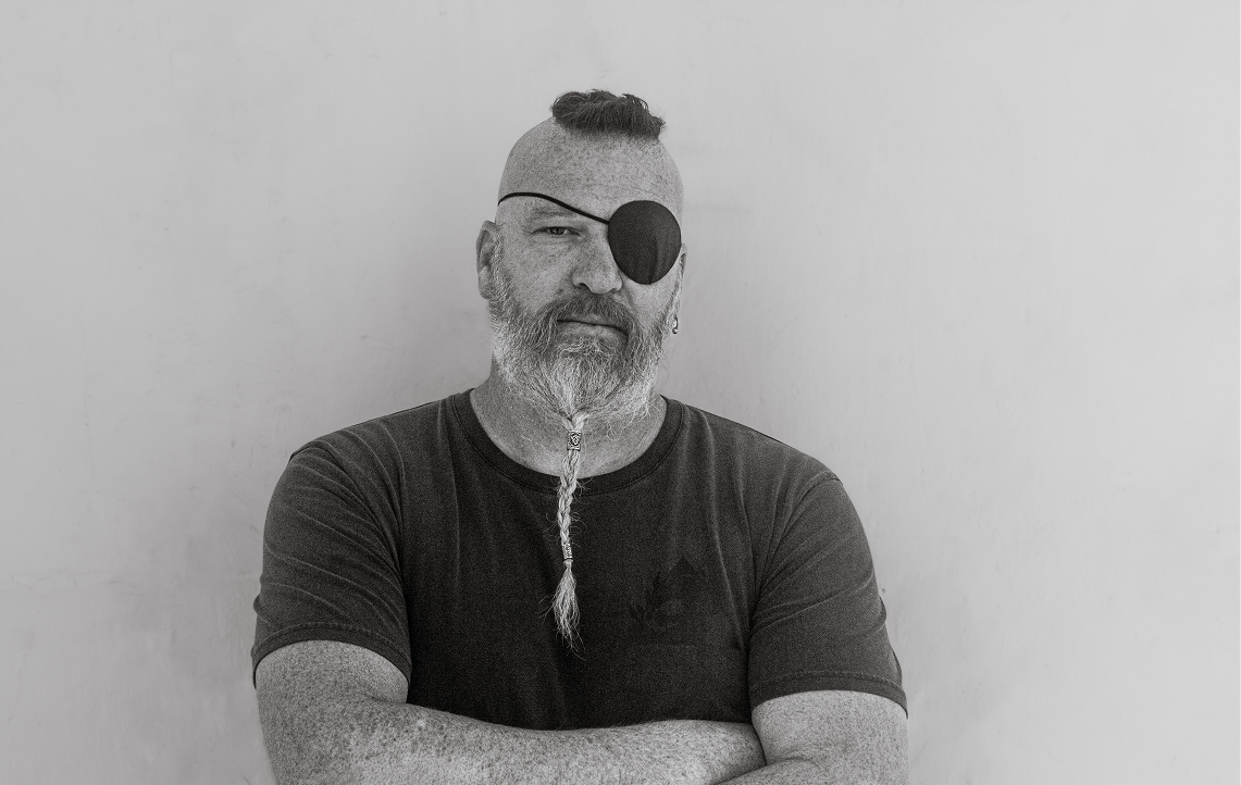Man with a beard and eye patch wearing black Canara Famous shirt